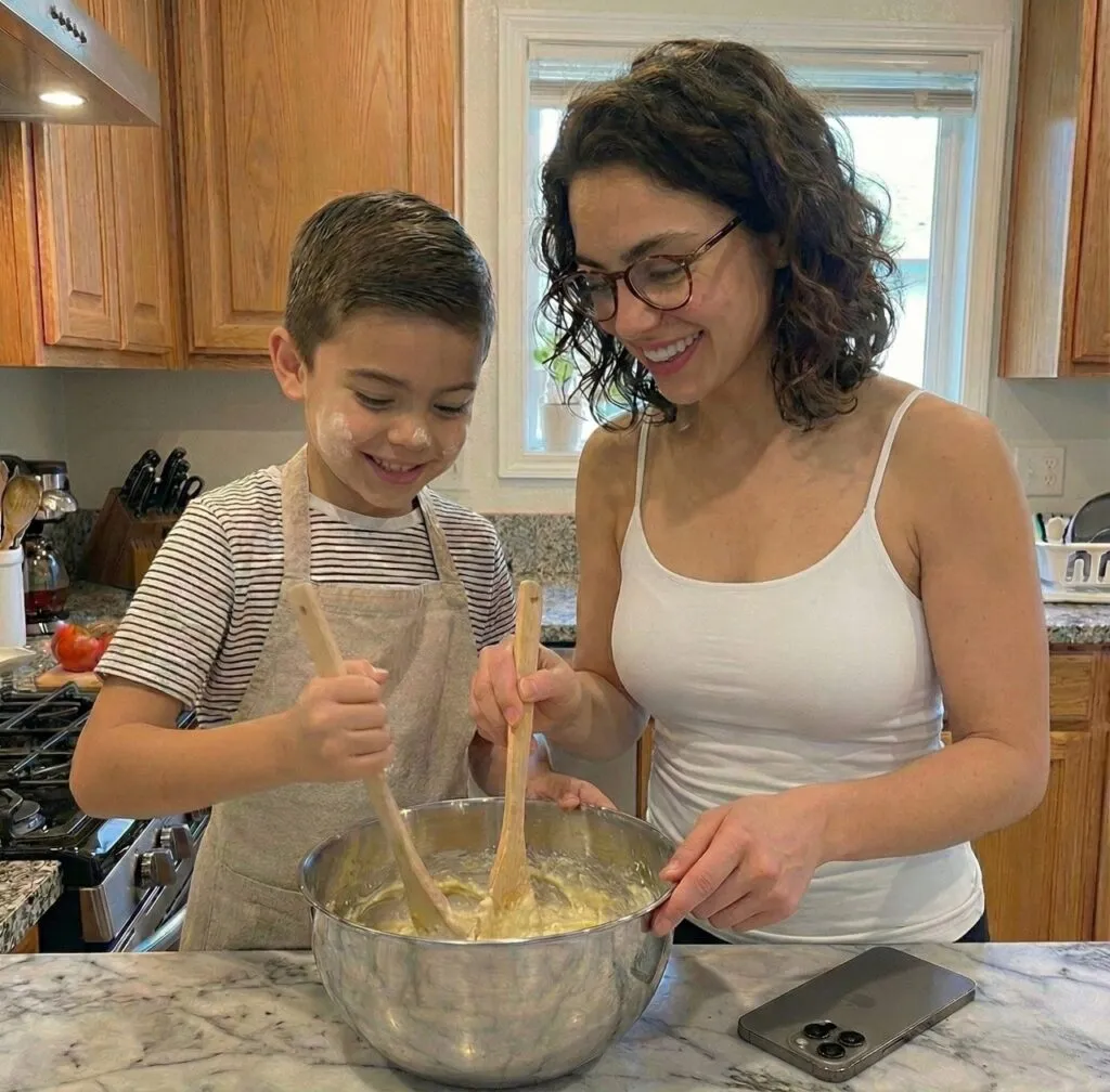 Aliana and a young boy smiling while mixing batter together in a kitchen.