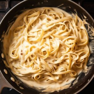 Fettuccine pasta coated in creamy Alfredo sauce with melted Parmesan in a skillet