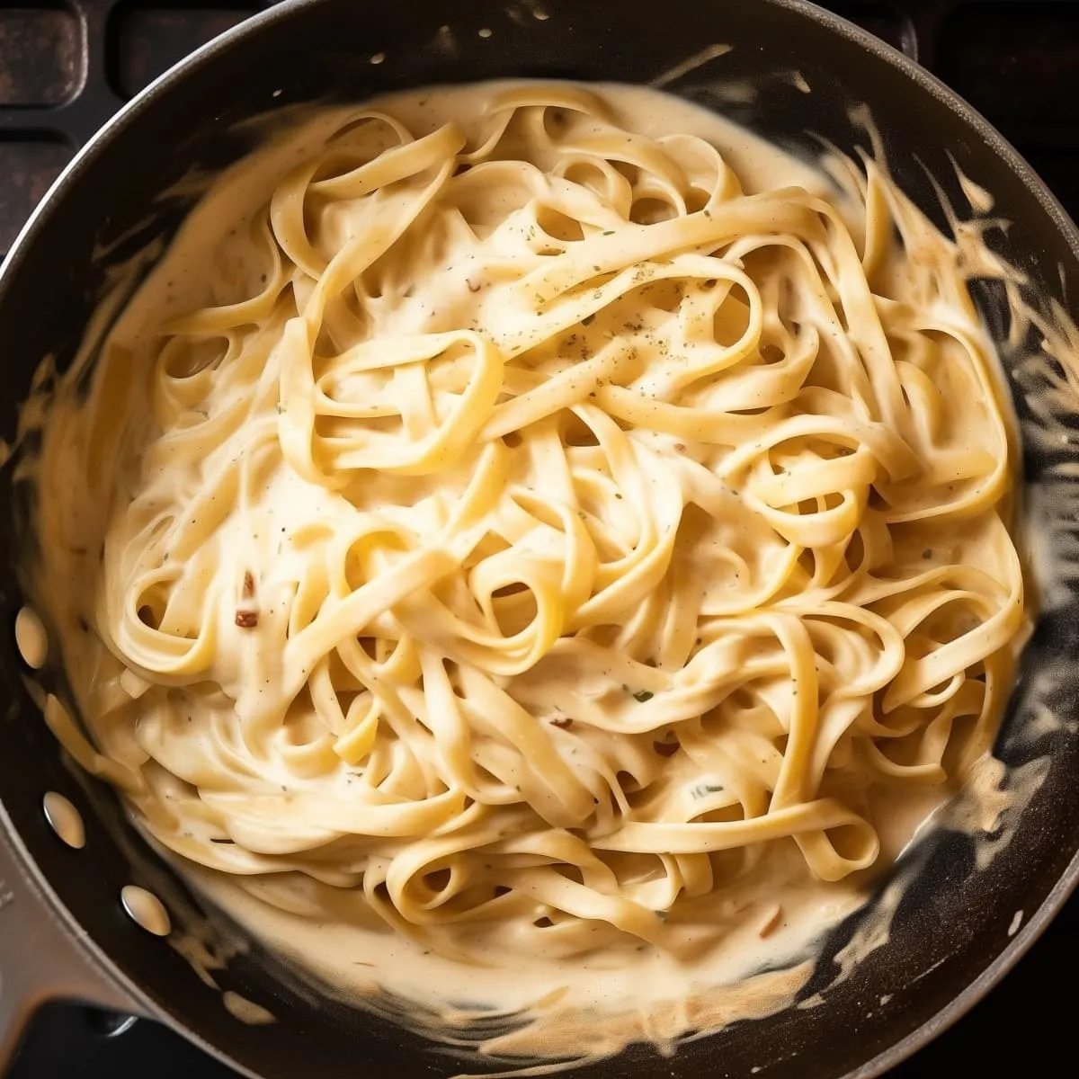 Fettuccine pasta coated in creamy Alfredo sauce with melted Parmesan in a skillet