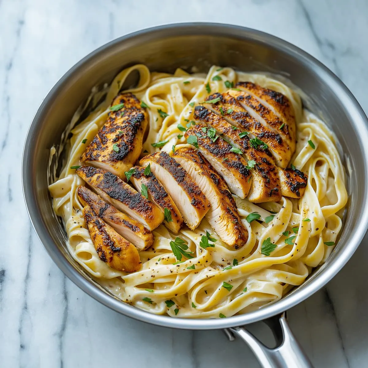Blackened chicken Alfredo served in a skillet with creamy fettuccine and fresh parsley