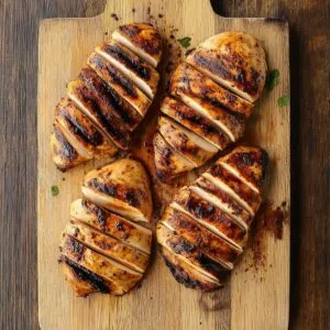 Cooked blackened chicken breasts sliced on a wooden cutting board with dark crust