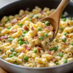 Creamy Ditalini Pasta Recipe with bacon and peas served hot in a skillet, lifted with a wooden spoon.