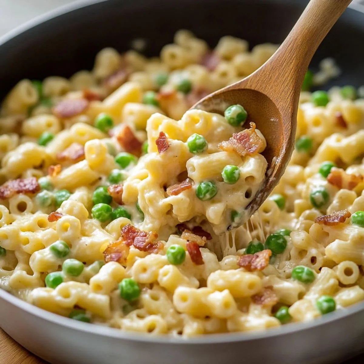 Creamy Ditalini Pasta Recipe with bacon and peas served hot in a skillet, lifted with a wooden spoon.