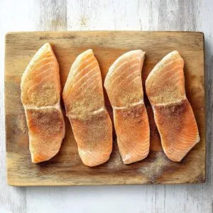 Raw chicken fillets seasoned with spices on a wooden cutting board