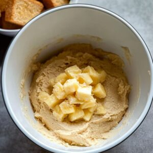 Crushed pineapple added on top of whipped butter and sugar in a mixing bowl, ready to be mixed