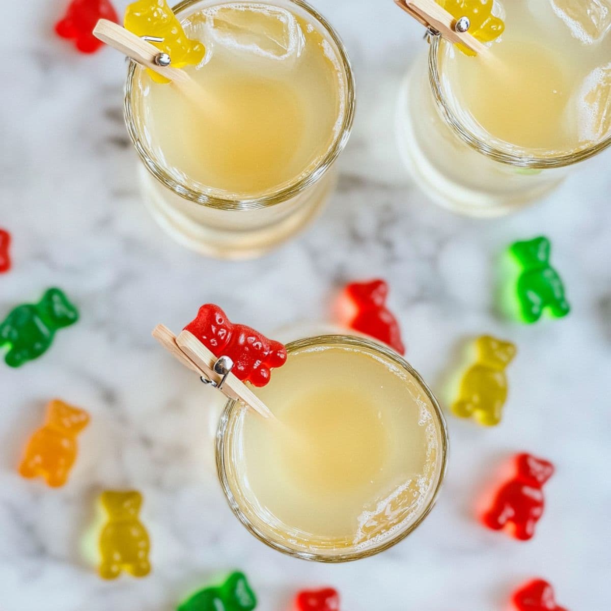 Overhead view of gummy bear shots with red and yellow bears clipped to the rims on a marble surface