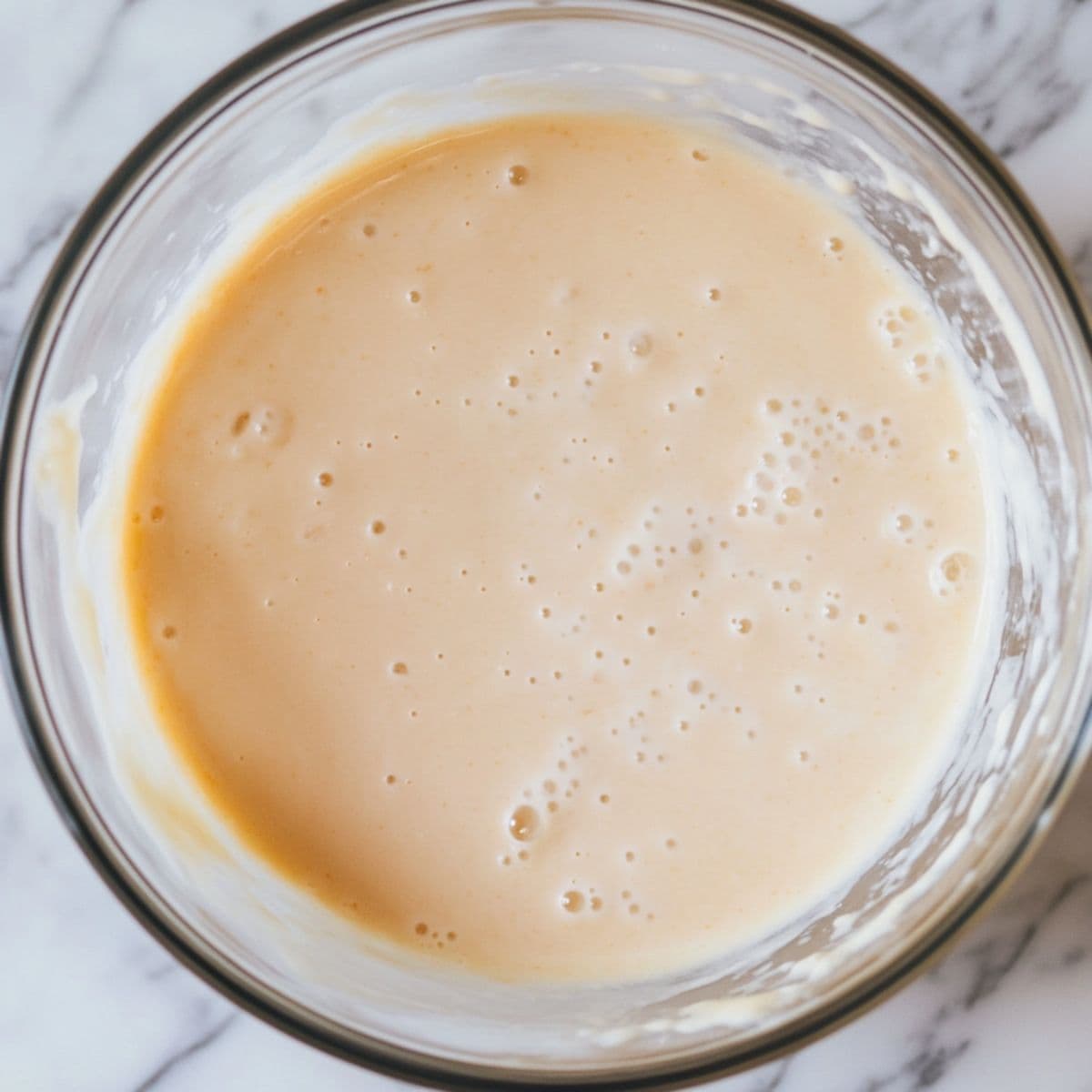 Bowl of pale, lightly curdled muffin batter after mixing in wet ingredients like sour cream and eggs.