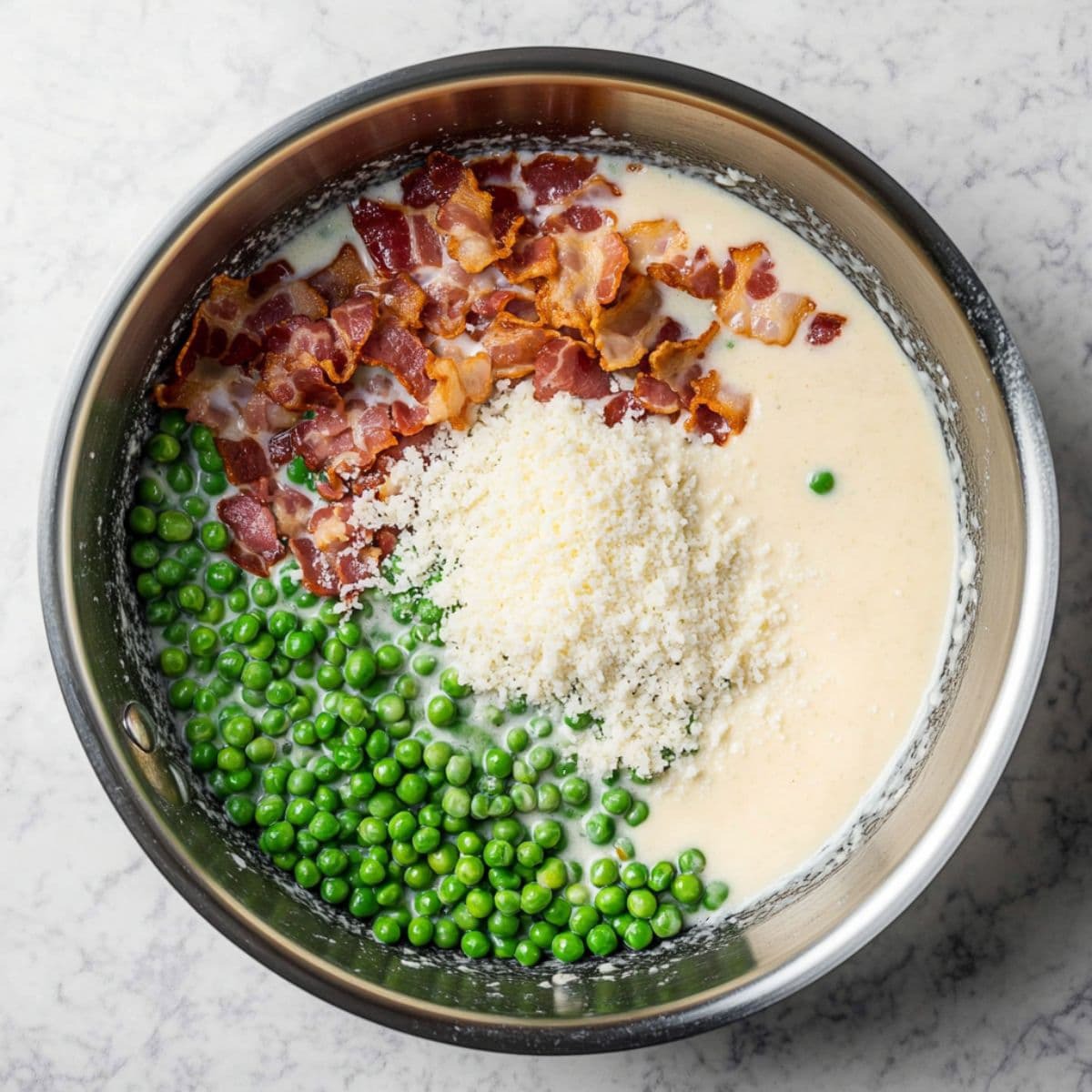 Creamy sauce base with crispy bacon, peas, and Parmesan cheese in a skillet before mixing.