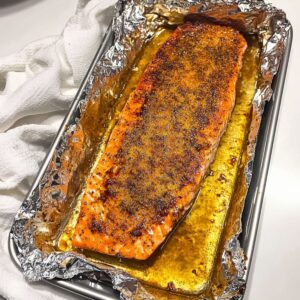 Baked salmon fillet in foil-lined tray with caramelized crust and melted butter