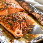 Fork flaking a juicy baked salmon fillet with golden crust and melted garlic butter