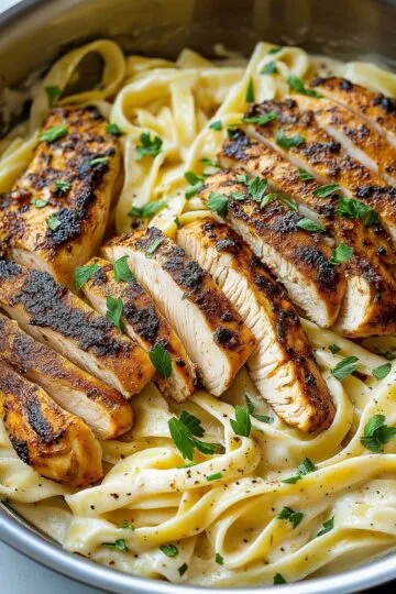 Blackened chicken Alfredo with creamy fettuccine in a skillet, garnished with parsley