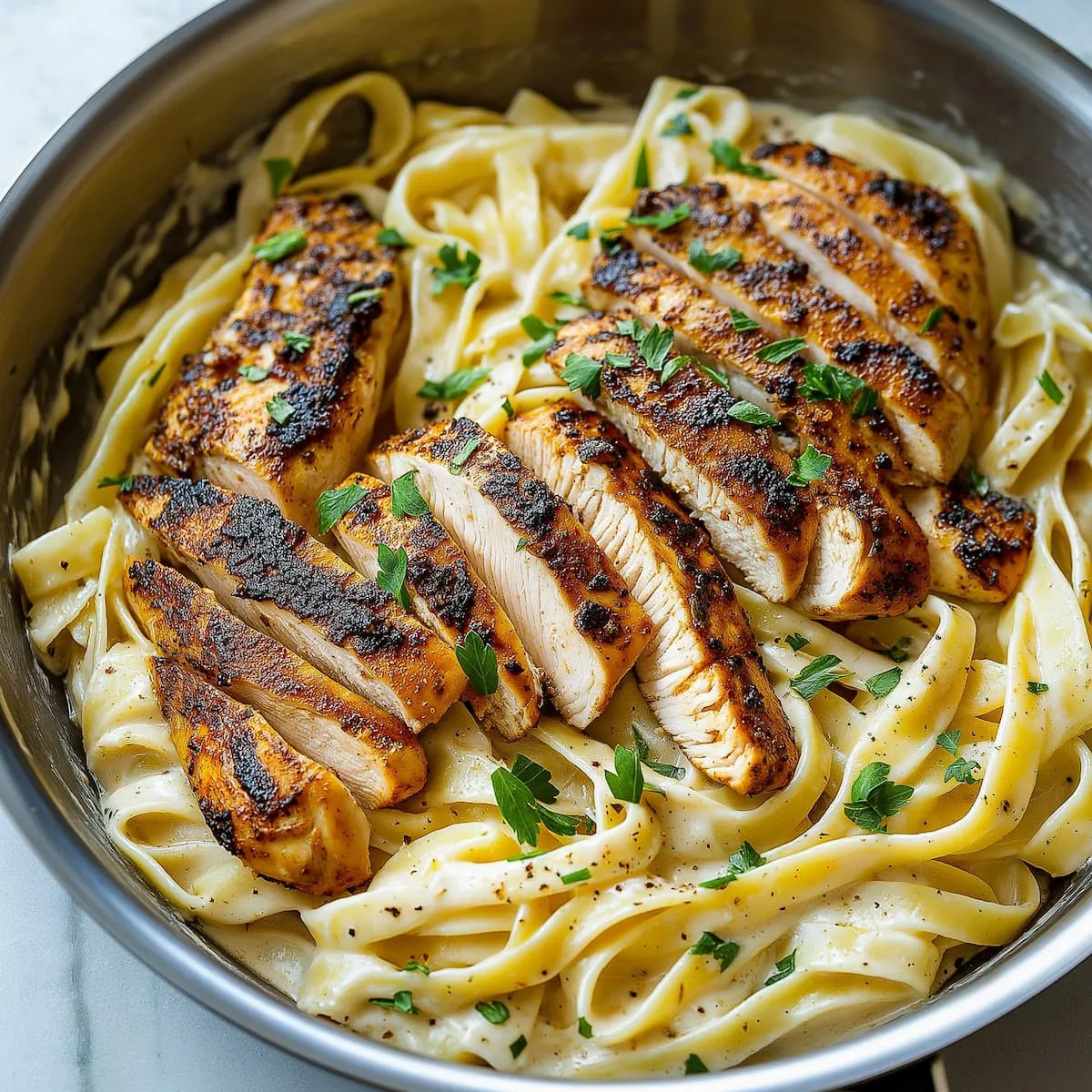 Blackened chicken Alfredo with creamy fettuccine in a skillet, garnished with parsley