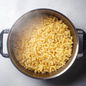 Steaming pot of freshly boiled ditalini pasta, cooked al dente in a stainless steel pot.