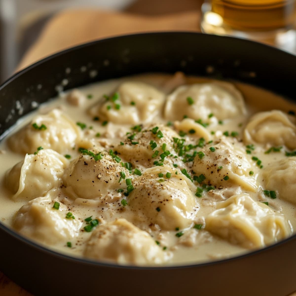 Creamy dumplings simmering in a pot, topped with chopped chives and pepper.