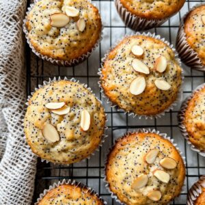 Almond poppy seed muffins cooling on a wire rack with golden tops and sliced almonds.