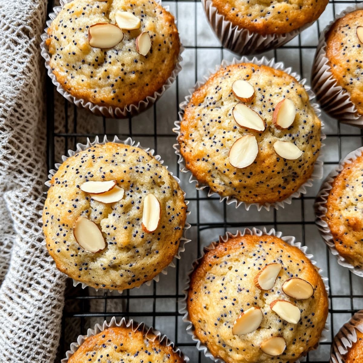 Almond poppy seed muffins cooling on a wire rack with golden tops and sliced almonds.