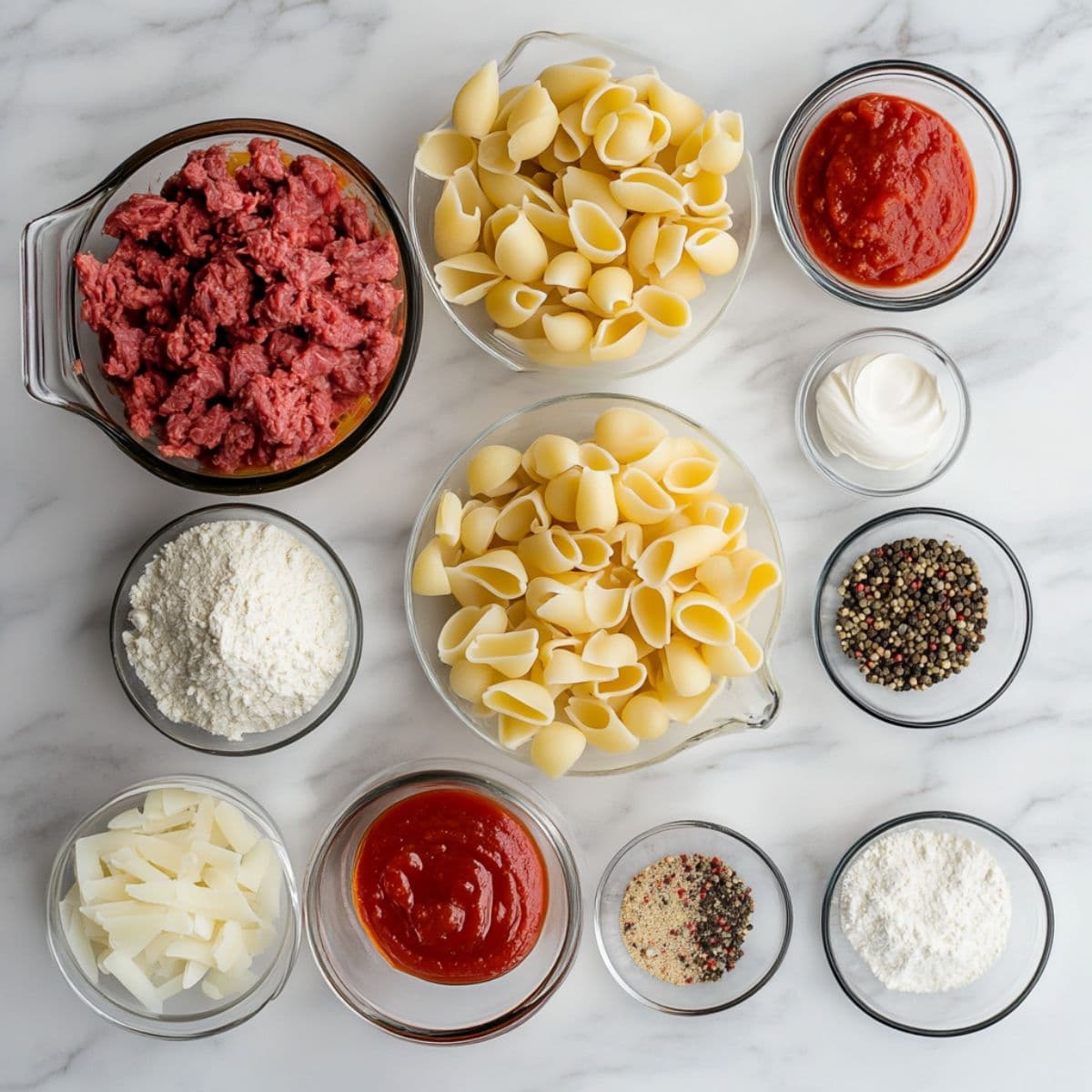 Overhead image of raw ingredients for creamy beef and shells arranged on a white marble countertop.