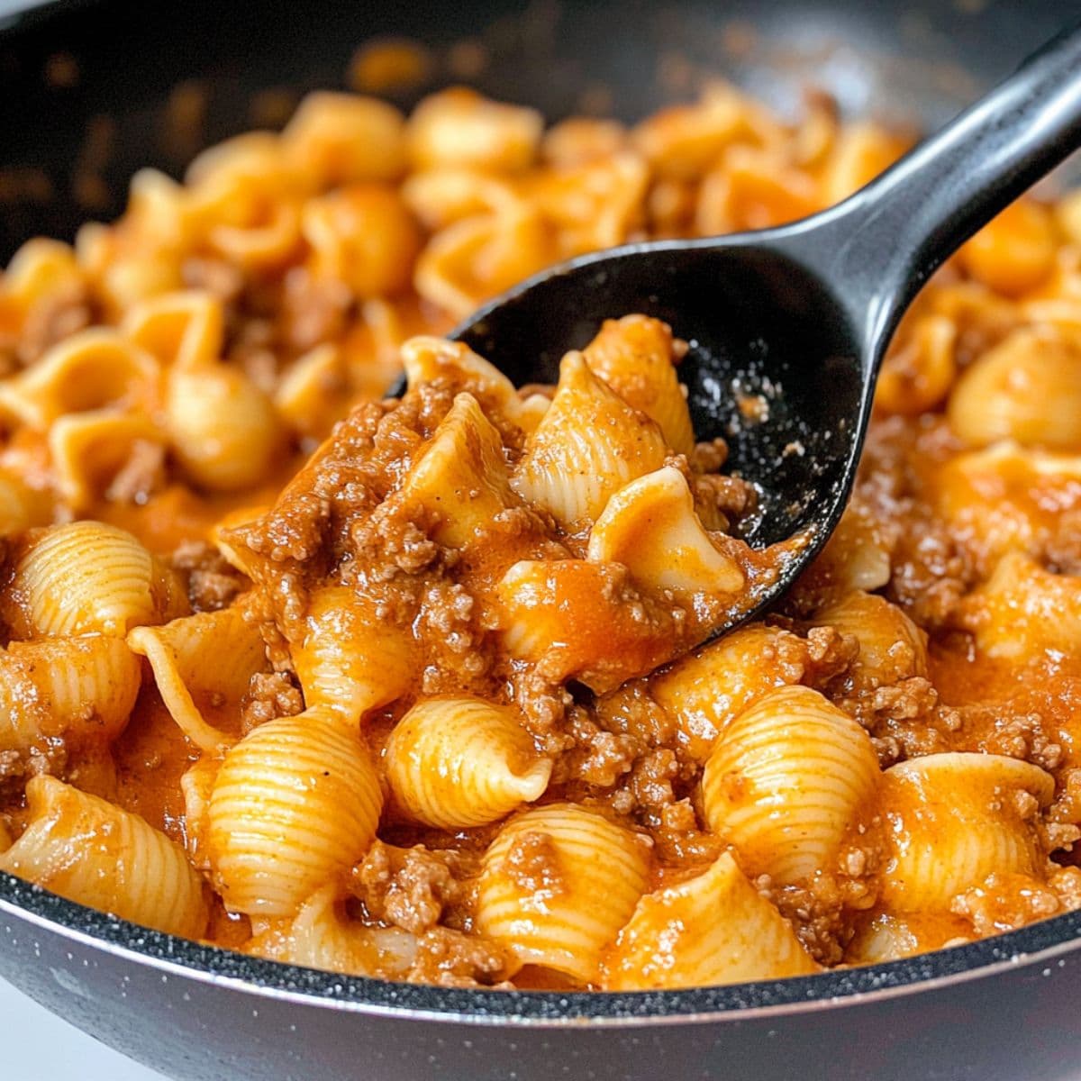Close-up shot of creamy beef and shells being scooped with a spoon from a skillet.