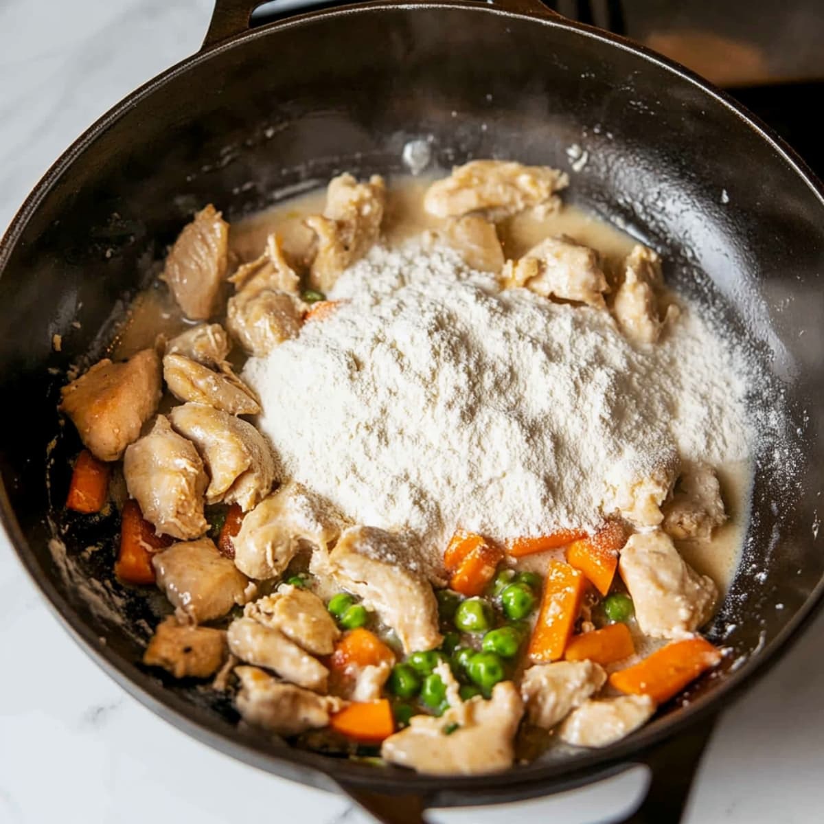 Flour sprinkled over chicken, carrots, and peas in a black Dutch oven, beginning the creamy sauce base.