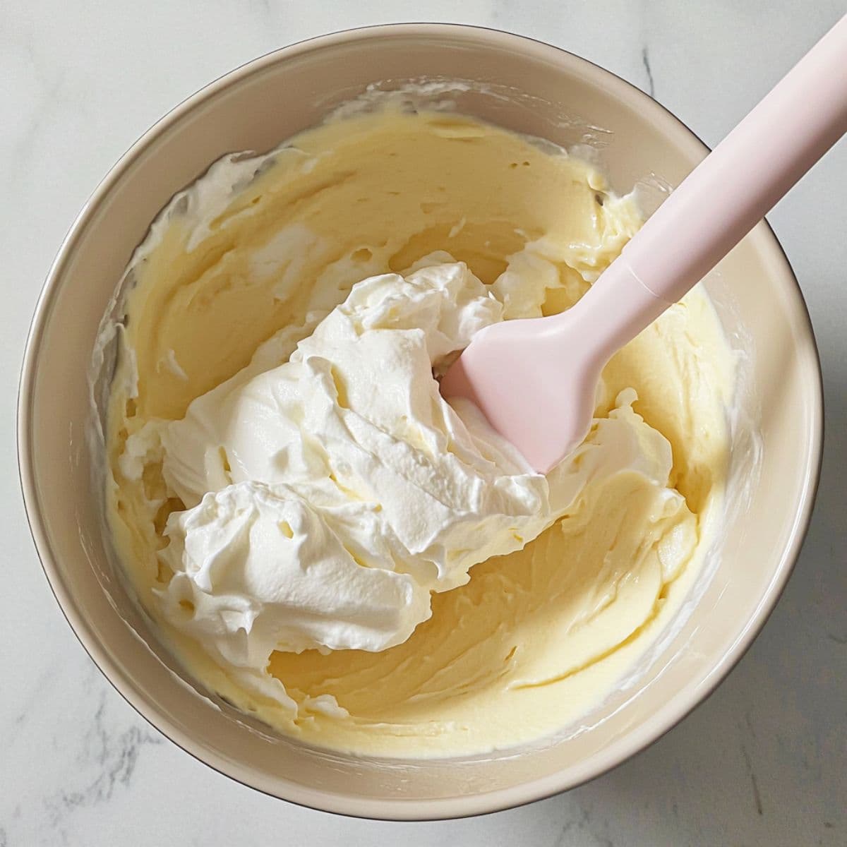Whipped topping being folded into vanilla pudding with pink spatula.