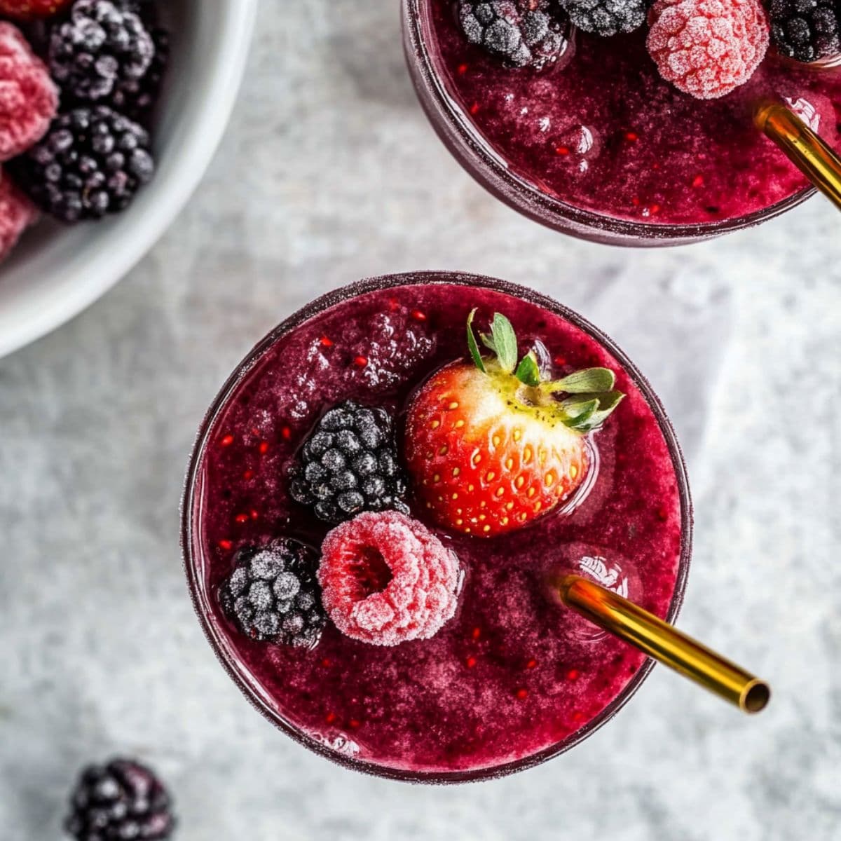 Frozen berry slushies garnished with fruit and gold straws