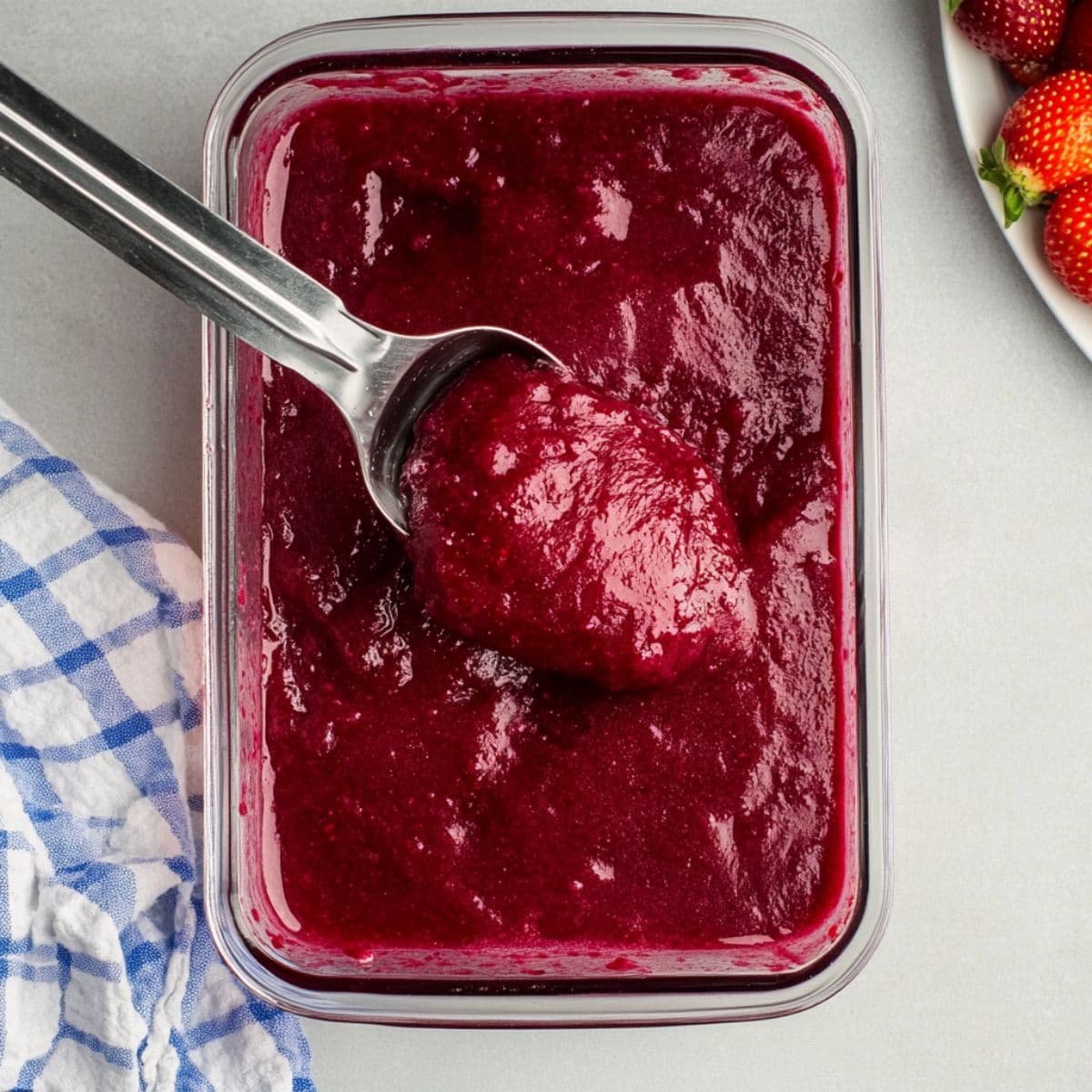 Scooping frozen berry slush from a glass container