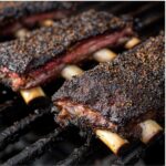 Beef back ribs cooking on grill with dark spice crust and bone tips