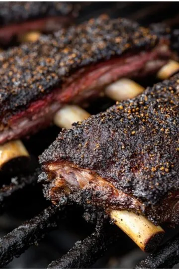 Beef back ribs cooking on grill with dark spice crust and bone tips