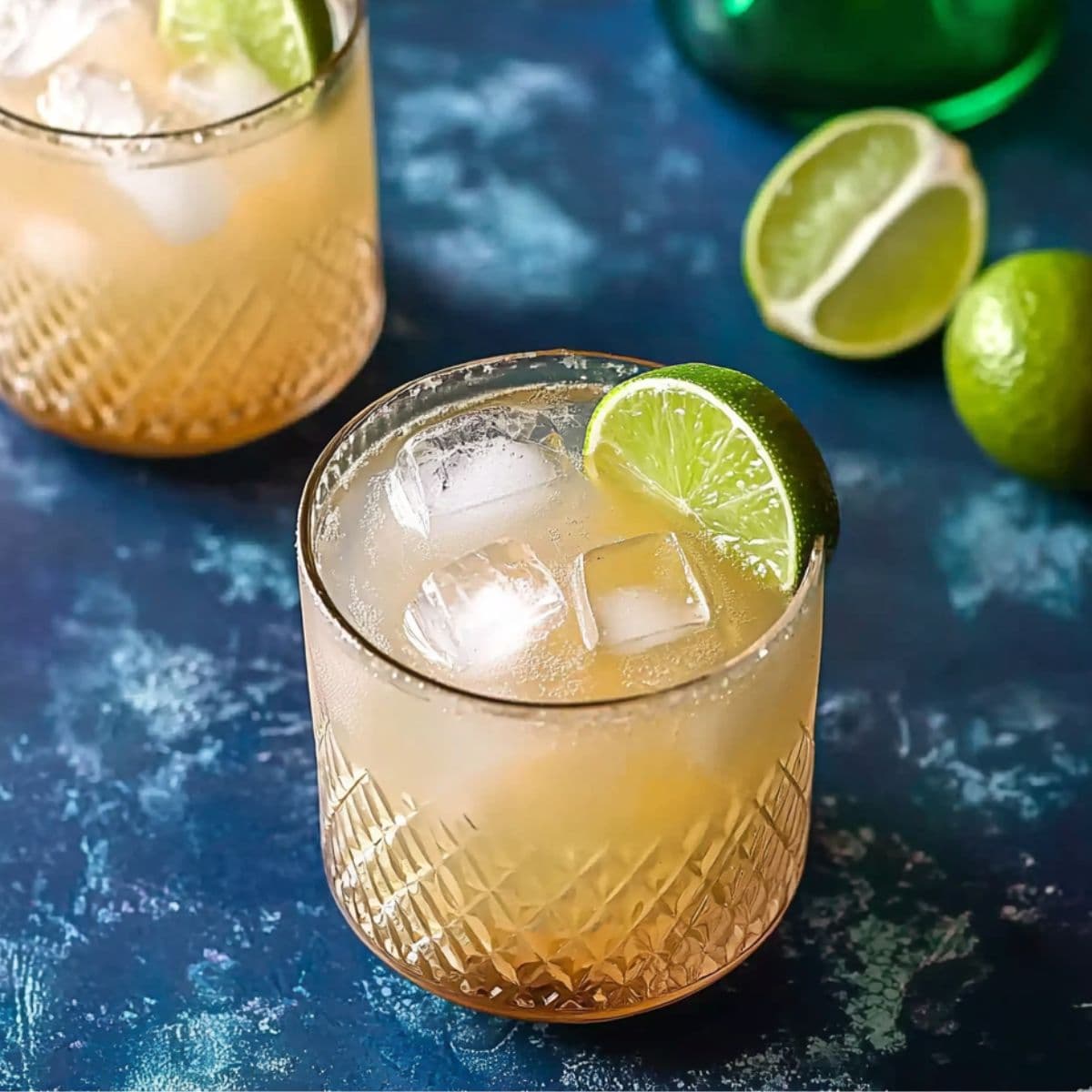 Two Kentucky Mule cocktails with lime wedges on a blue surface