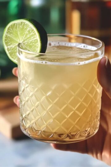 Hand holding a Kentucky Mule cocktail garnished with lime in a textured glass
