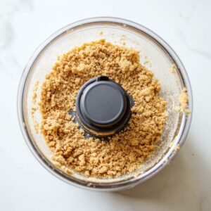 Food processor filled with blended graham cracker crust mixture for strawberry cheesecake ice cream.