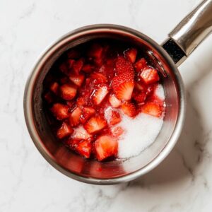 Diced strawberries with sugar in a stainless steel saucepan, beginning to cook into a homemade strawberry sauce.