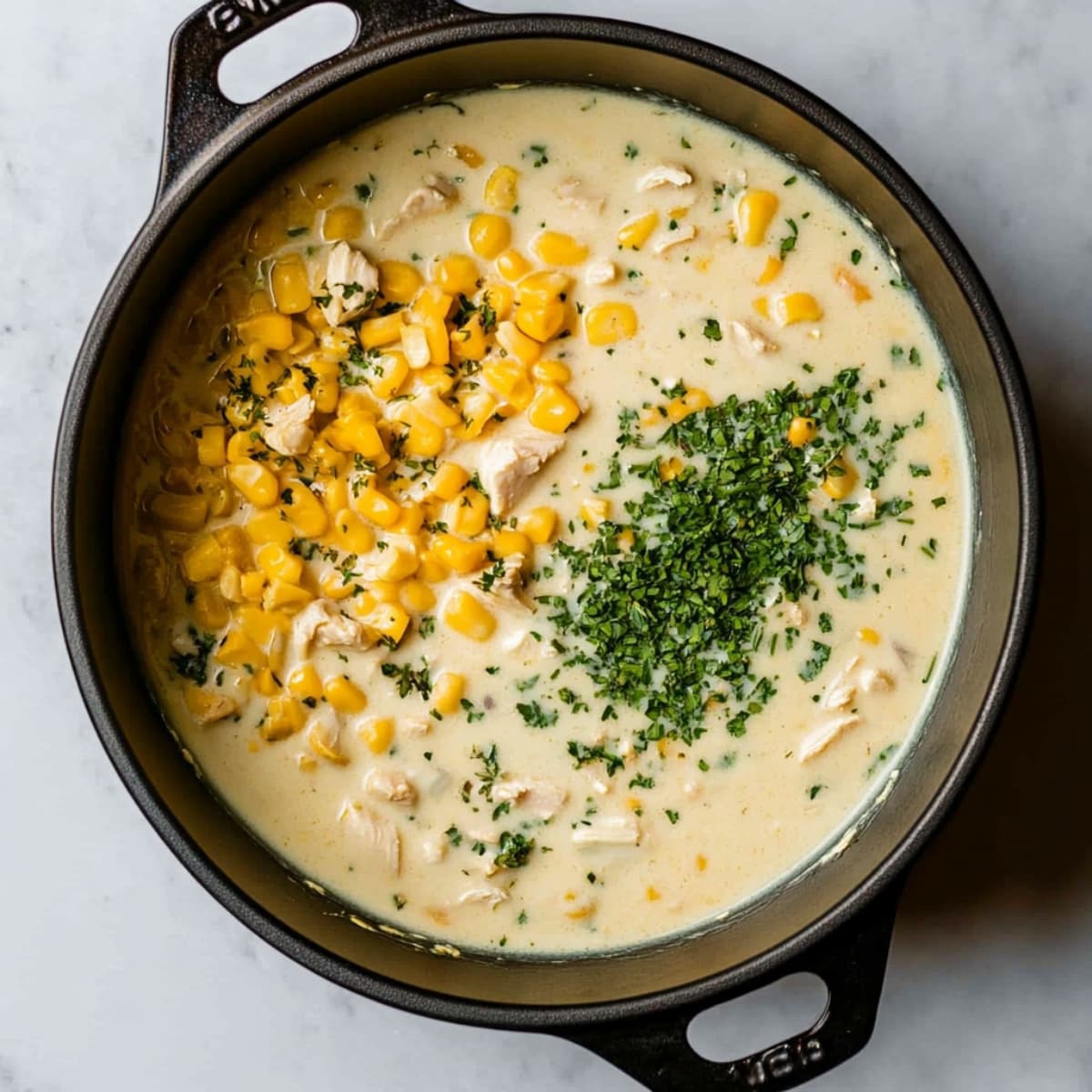 Creamy chicken and corn filling in a black Dutch oven with chopped parsley on top, ready to simmer.