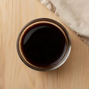 Glass bowl filled with dark soy sauce mix for Pad See Ew on a wooden surface.