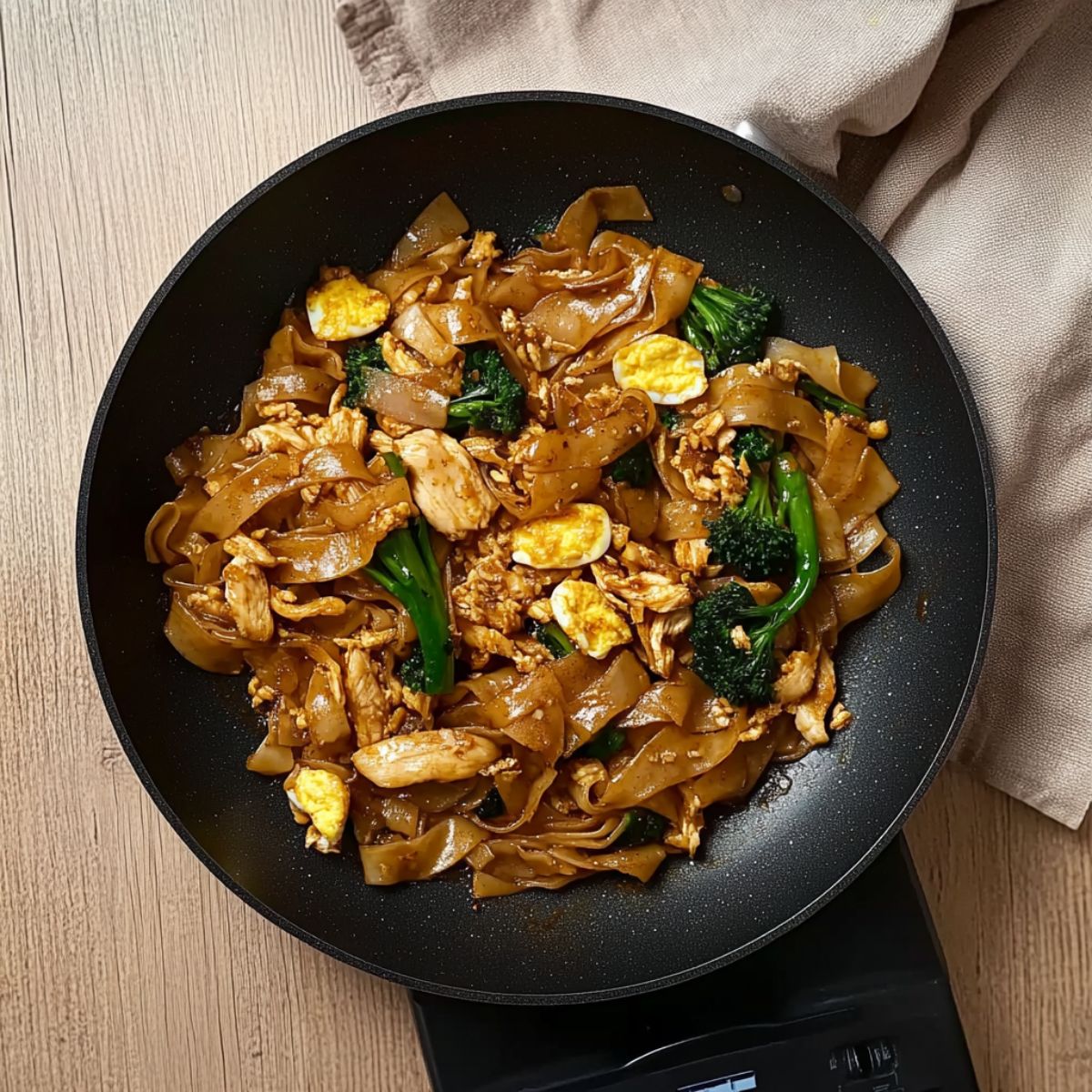 Cooked Pad See Ew with egg, chicken, and broccoli in a non-stick pan.