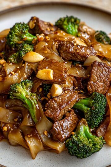 Pad See Ew with seared beef, broccoli, and noodles served on a ceramic plate with toasted garlic.