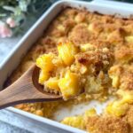 Golden pineapple stuffing on a wooden spoon with the baked dish in the background