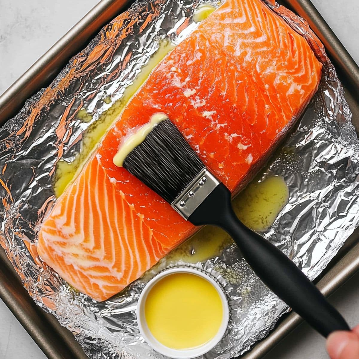 Brushing melted butter over raw salmon fillet on foil-lined tray