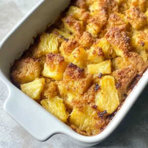Close-up of baked pineapple stuffing resting in a white dish with caramelized top