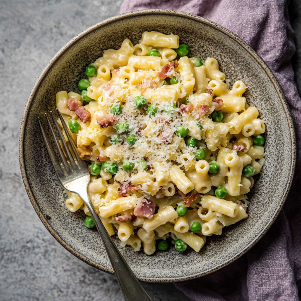 Bowl of creamy ditalini pasta with bacon, peas, and grated Parmesan, ready to serve with a fork.