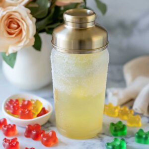 Frosted cocktail shaker filled with gummy bear shot mix and surrounded by gummy bears on marble
