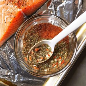 Bowl of mixed seasoning with spoon and raw salmon fillet in background