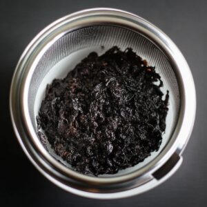 Fine mesh strainer filled with thick vanilla bean paste over a white bowl