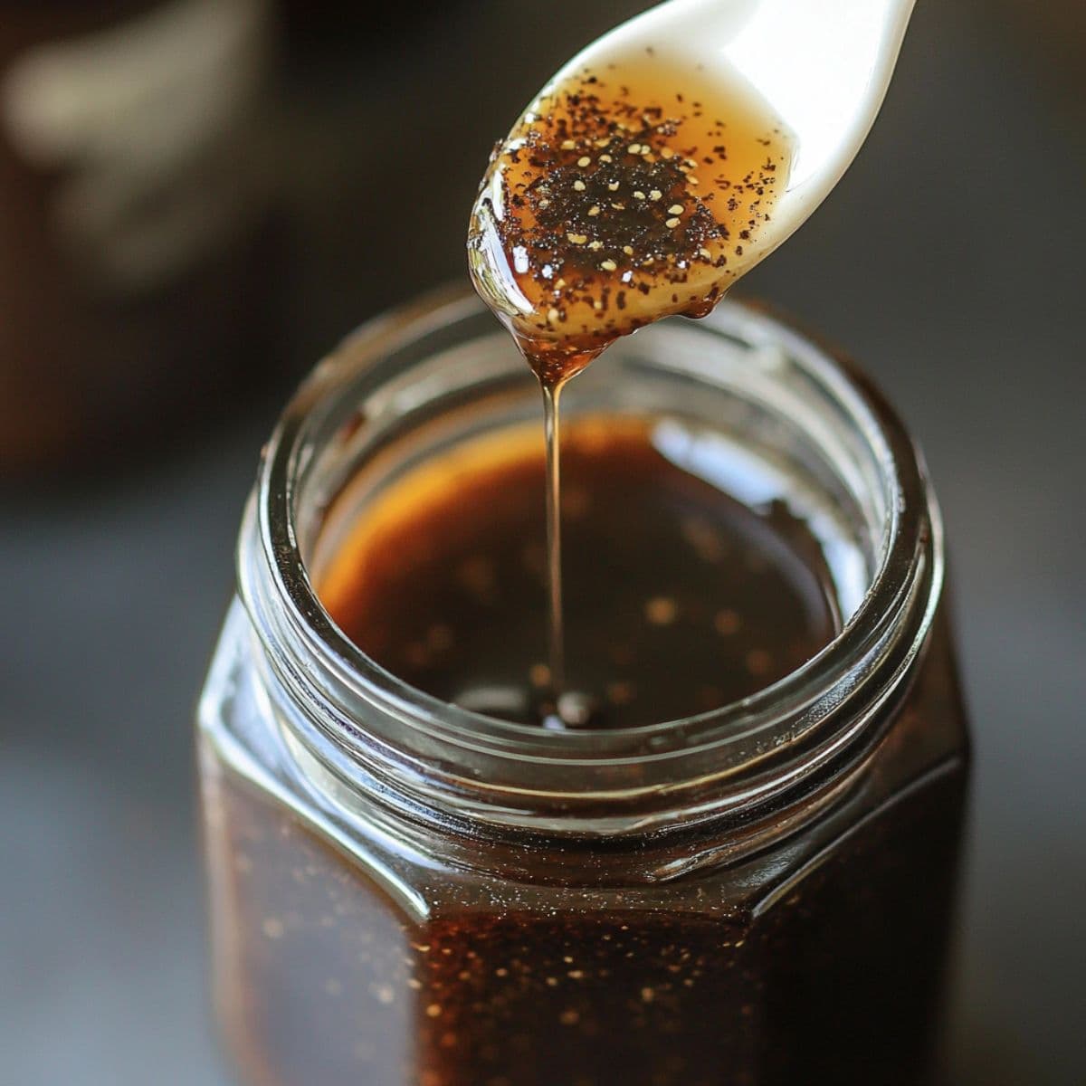 Spoon drizzling glossy vanilla bean paste into a glass jar