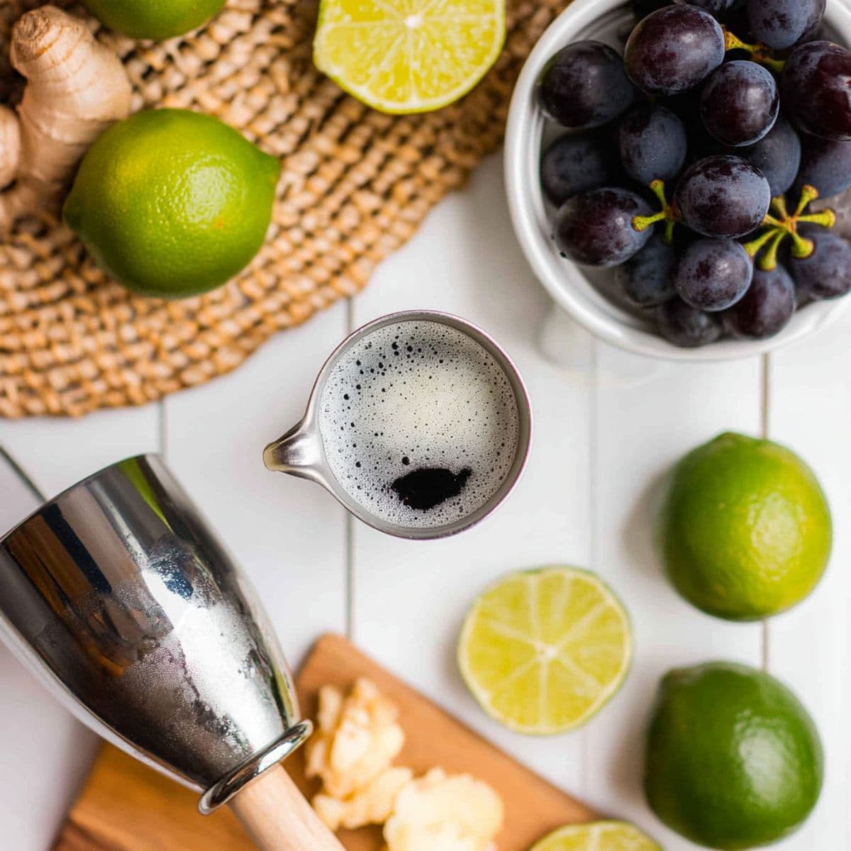 Flat lay of fresh ingredients for a Transfusion cocktail – grapes, limes, ginger, and cocktail tools