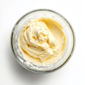 Whipped cream with stiff peaks in a glass bowl, ready for folding into cheesecake ice cream mixture.