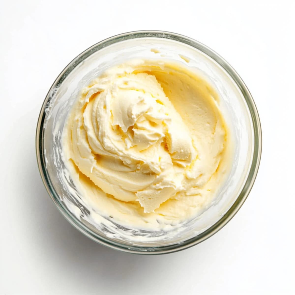 Whipped cream with stiff peaks in a glass bowl, ready for folding into cheesecake ice cream mixture.