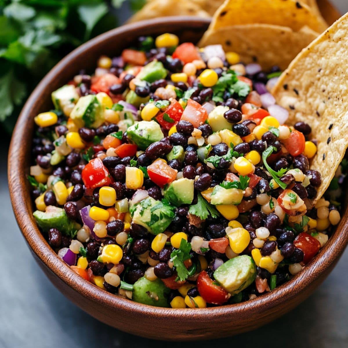 Cowboy caviar served in wooden bowl showing colorful mixture of black beans, corn, tomatoes, and fresh herbs with tortilla chips