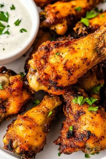 Ultimate air fryer chicken wings with perfect golden brown crispy skin being held showing incredible seasoning and ranch dipping sauce on white plate