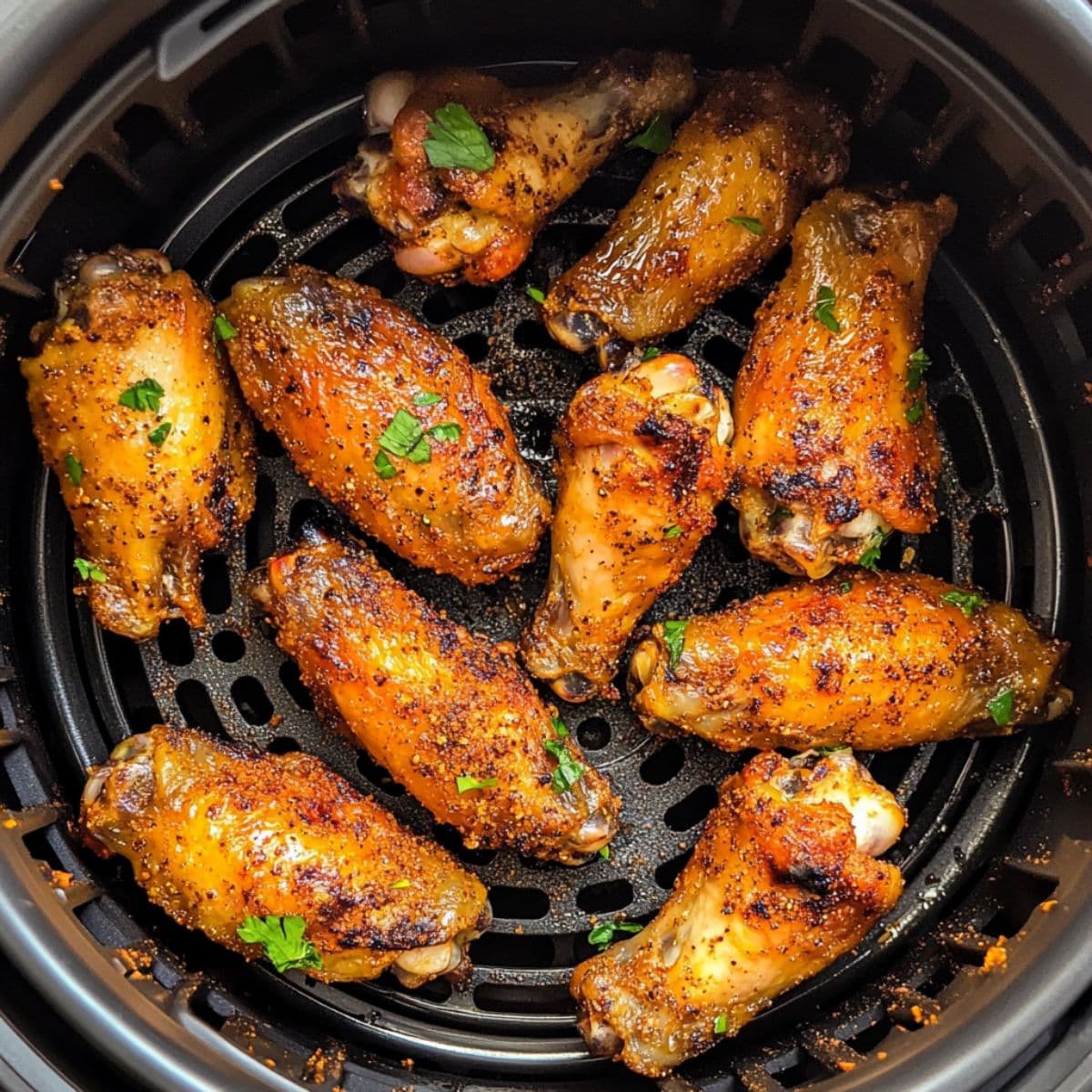 Air fryer chicken wings cooking in air fryer basket showing golden brown crispy skin with perfect seasoning and fresh herb garnish during cooking process
